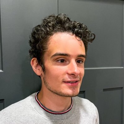 carter temm smiles into the distance, wearing a sweatshirt with his hair swept to the side